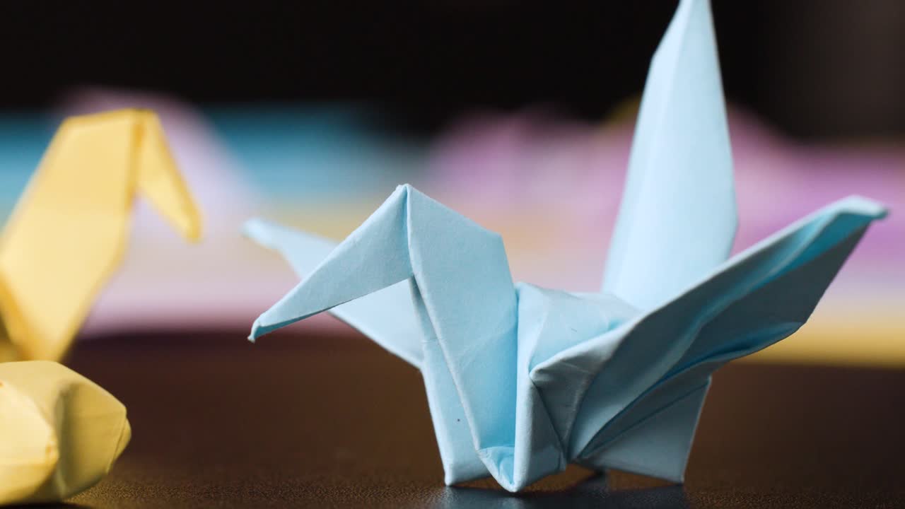 Un primo piano cattura delle mani che piegano meticolosamente un origami a forma di gru di carta blu su una superficie scura