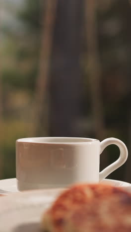 coffee cup on served table closeup. white ceramic mug of hot drink and dishes for breakfast in kitchen. refreshing beverage and food indoors