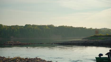 men rowing the boat on shore. sunset on the river with verdant forest in the background.