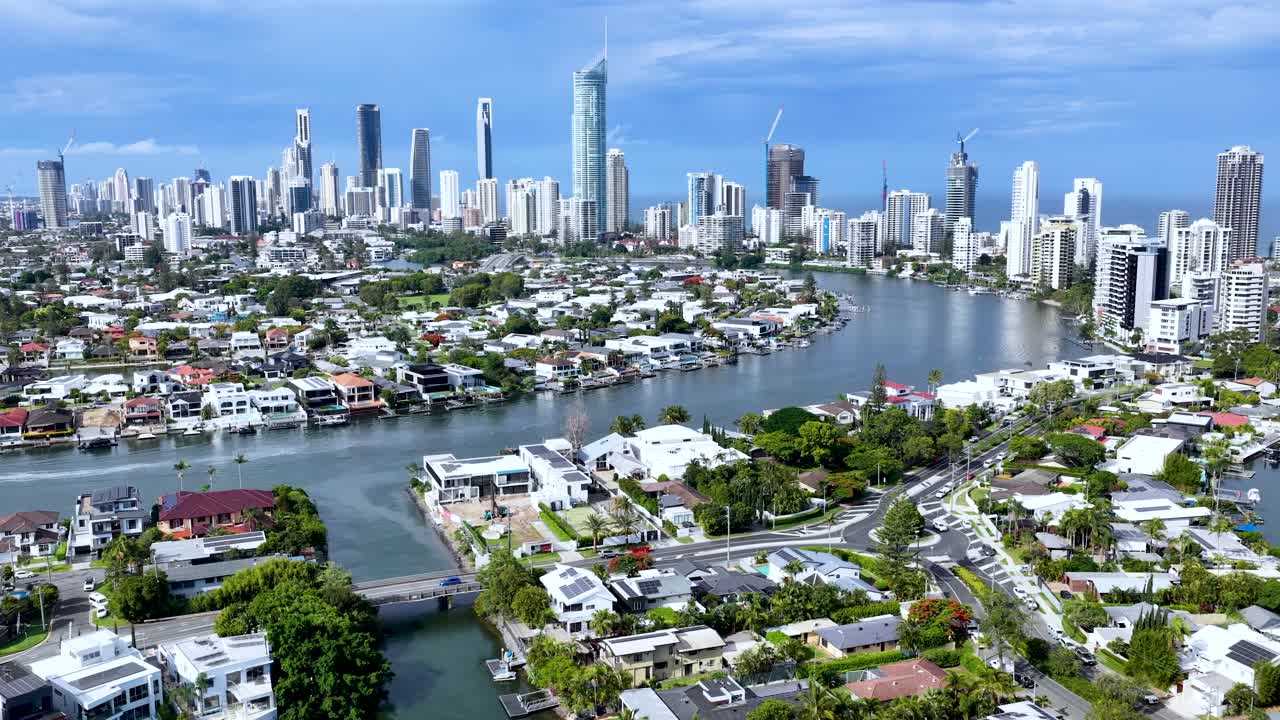 Drone glides above Gold Coast canals, luxury homes, and skyline under bright daylight, smooth movement