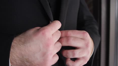 novio usando sus manos para ajustar su traje negro durante su día de la boda
