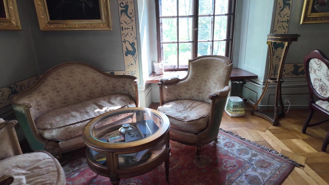 Historic gallery interior featuring vintage sofas, carved table, decorative chairs and artwork displayed on soft blue walls.