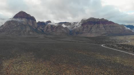 aerial drone shot of an empty highway next to mountains with low clouds