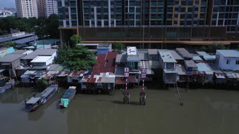 Aerial-view-on-Kenh-Te-canal-Ho-Chi-Minh-City-with-old-iron-and-wood-shacks,-traditional-river-boats-and-ultra-modern-high-rise-buildings-on-sunny-day