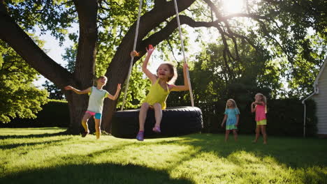 girls playing on a tire swing in a sunny backyard
