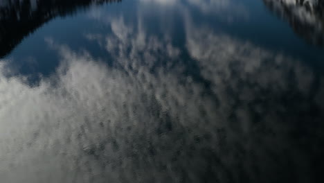 inclínate hacia arriba desde una nube que refleja la bahía esmeralda hasta las montañas cubiertas de nieve y el cielo azul