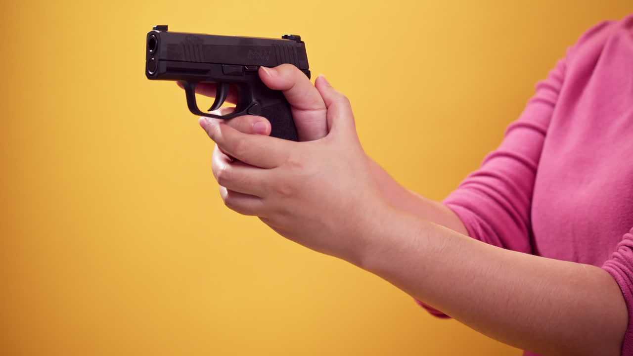 Close up woman holds a handgun to aim the gun on bright yellow background