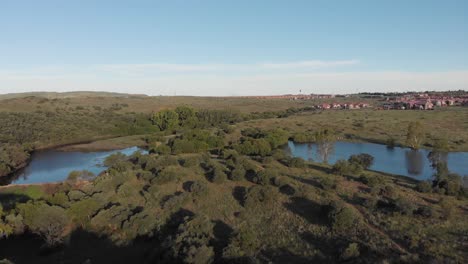 Toma-Aérea-Inversa-De-Una-Presa-En-Un-Valle-Verde-Con-Vivienda-En-La-Parte-Posterior