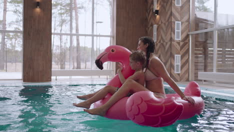 family weekend in water park mother with child are floating on inflatable pink flamingo