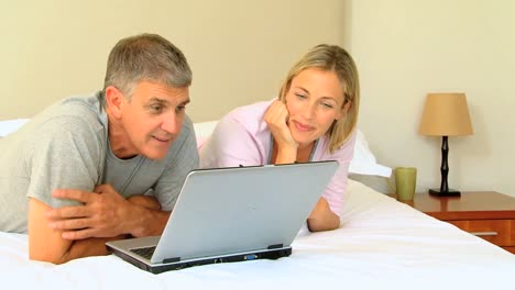 una pareja relajándose en la cama con una computadora portátil