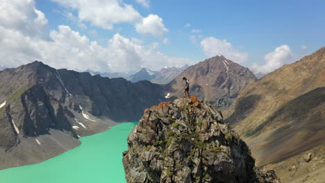 aerial circling drone shot of a man standing on a mountain top overlooking the ala-kol mountains, kyrgystan