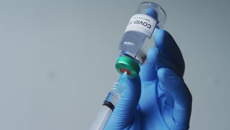 caucasian male doctor wearing protective gloves filling syringe with covid-19 vaccine