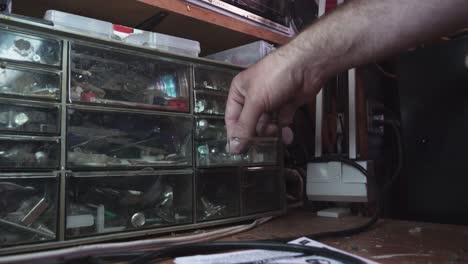 hombre agarrando hardware de un contenedor de almacenamiento de tuercas y tornillos dentro de un garaje