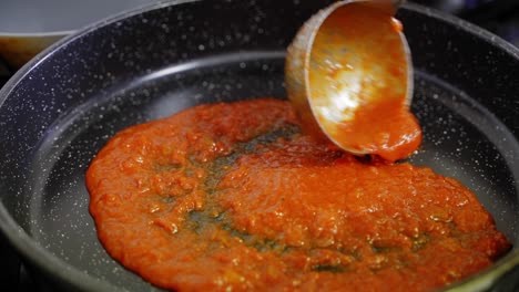 slow motion close-up of a ladle of tomato sauce being added to a frying pan