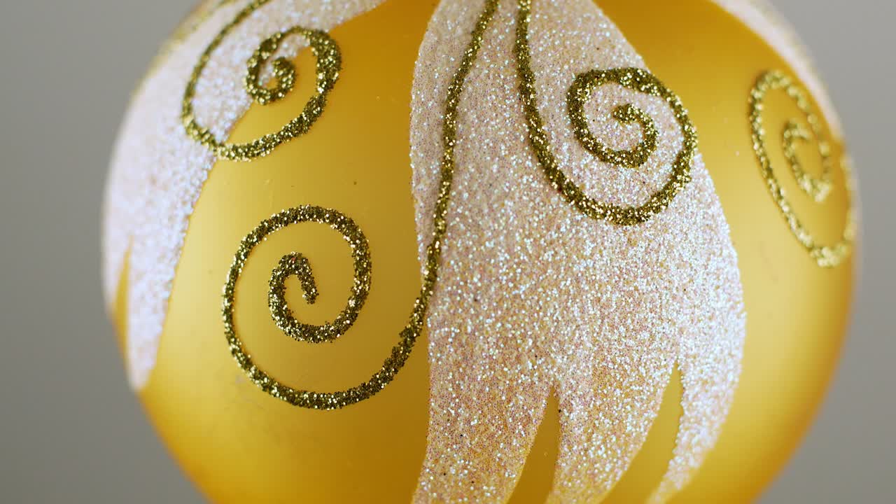 Golden Christmas ball toy turning round and back in luminous light on dark green background. New Year pattern.