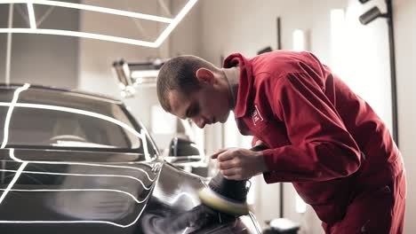 Hardworking-male-autocenter-represantative-polishing-intensly-new-black-car.