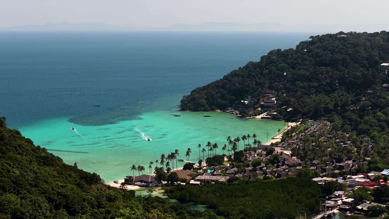 Inquadratura d'apertura di una baia di un'isola tropicale, con un resort di lusso immerso tra le fitte colline verdi