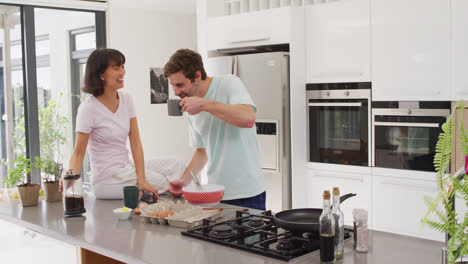 Video-of-happy-diverse-couple-drinking-coffee-together-in-kitchen