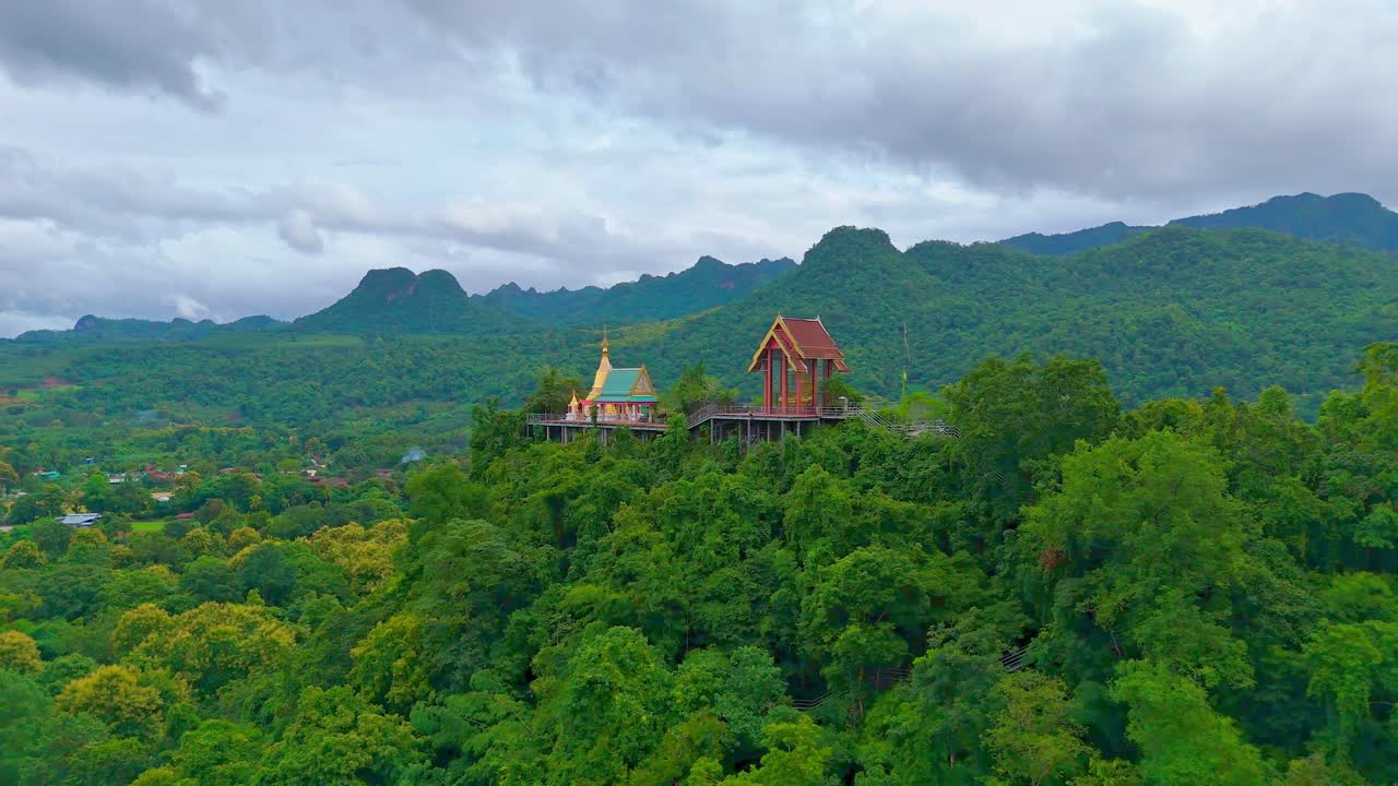 ภาพมุมสูงแบบวงโคจรของวัดพุทธที่ตั้งอยู่บนยอดเขาที่มีป่าและมีภูเขาเป็นพื้นหลังใกล้สังขละบุรี ประเทศไทย