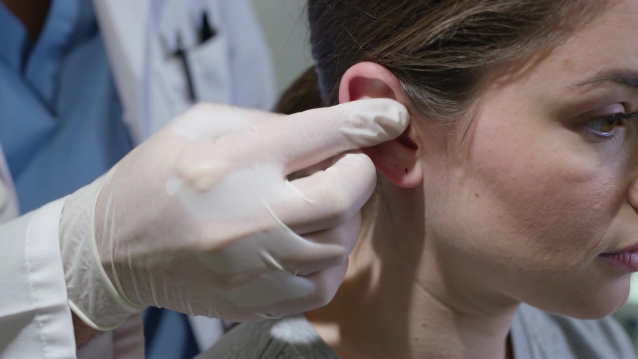 Clinico in camice che cammina, pulisce l'orecchio destro del paziente e controlla il piercing in clinica, con garza.