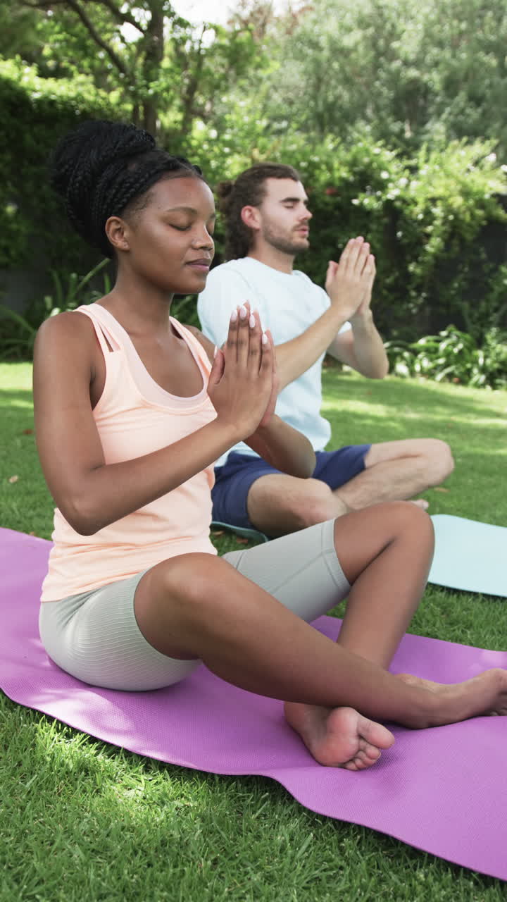 Vertical video: Diverse couple practicing yoga on purple mats at home