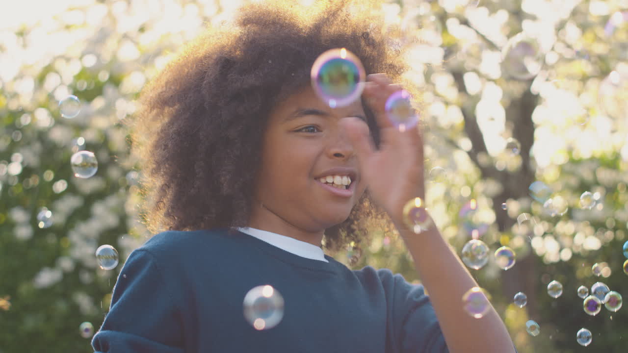Menino sorrindo ao ar livre divertindo-se brincando com bolhas no jardim