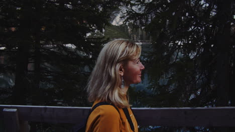 a blonde haired woman walks along the shore of the braies lake with a smile