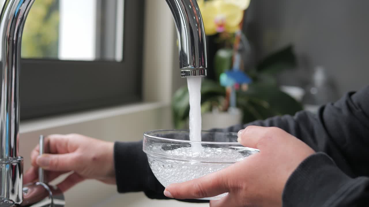 Close-up filling a glass bowl with water from the kitchen faucet