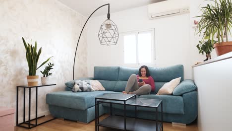 happy caucasian woman typing on her cell phone while sitting on her sofa