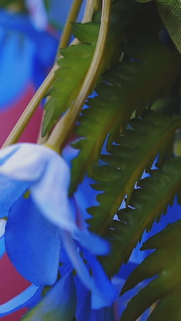 cu shot, slow motion: beautiful blue artificial flowers and green leaves hang near pink fabric on blurred background extreme close view