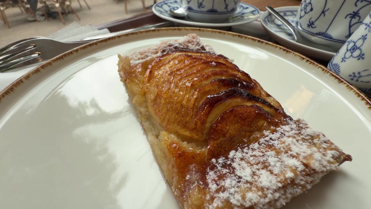 Apple tart slice with powdered sugar served on a plate at a cafe table setting