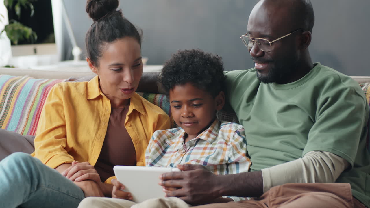 Famiglia afroamericana felice che usa un tablet digitale e parla sul divano di casa