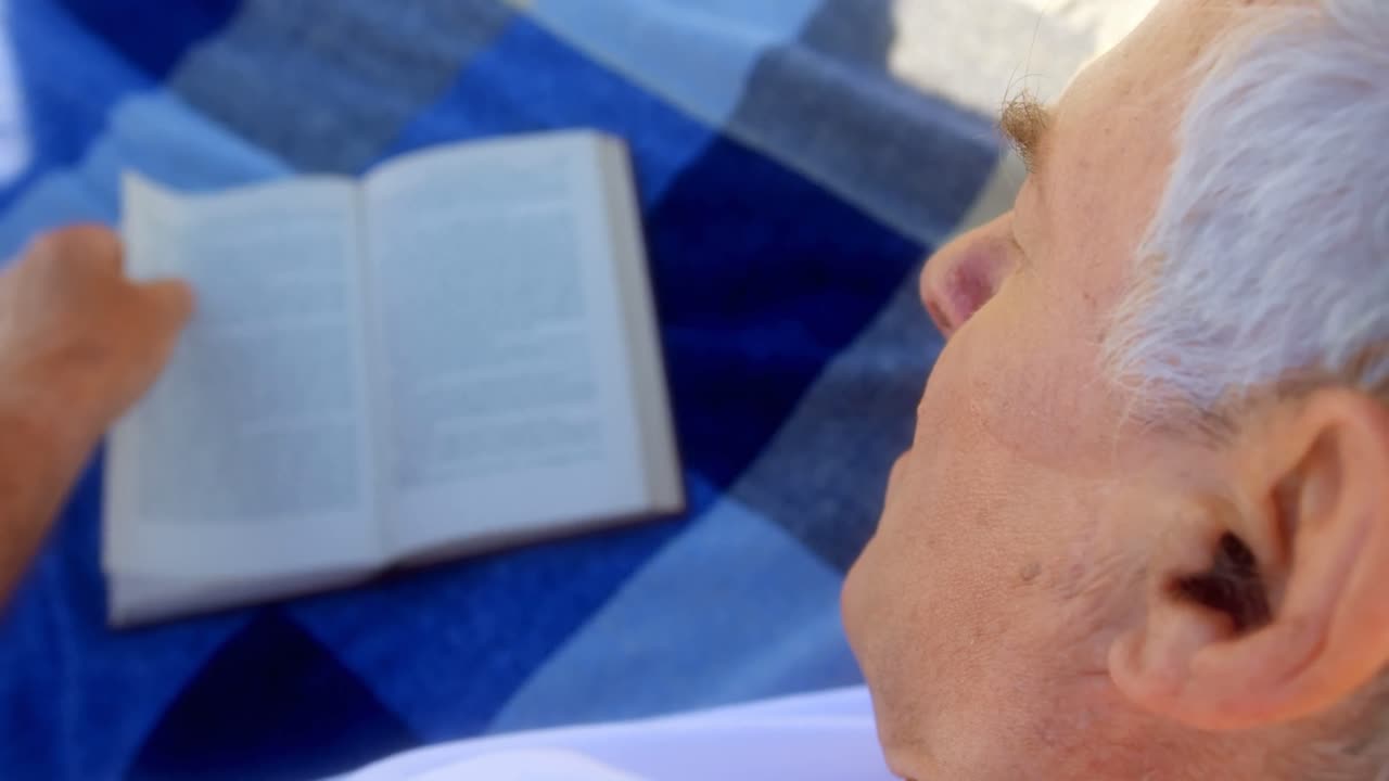 Primo piano di un uomo anziano caucasico attivo che legge un libro in spiaggia 4K
