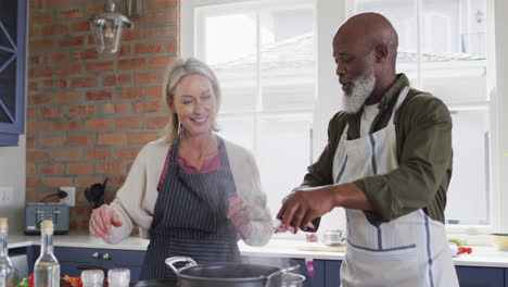 Mixed-race-couple-wearing-aprons-cooking-together-in-the-kitchen-at-home