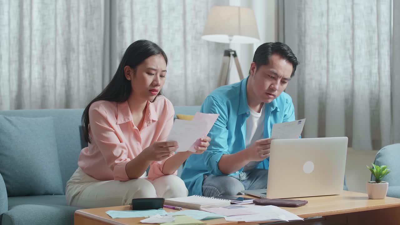 Asian Couple With A Laptop Looking At The Bill And Having Headache Due To Financial Problem
