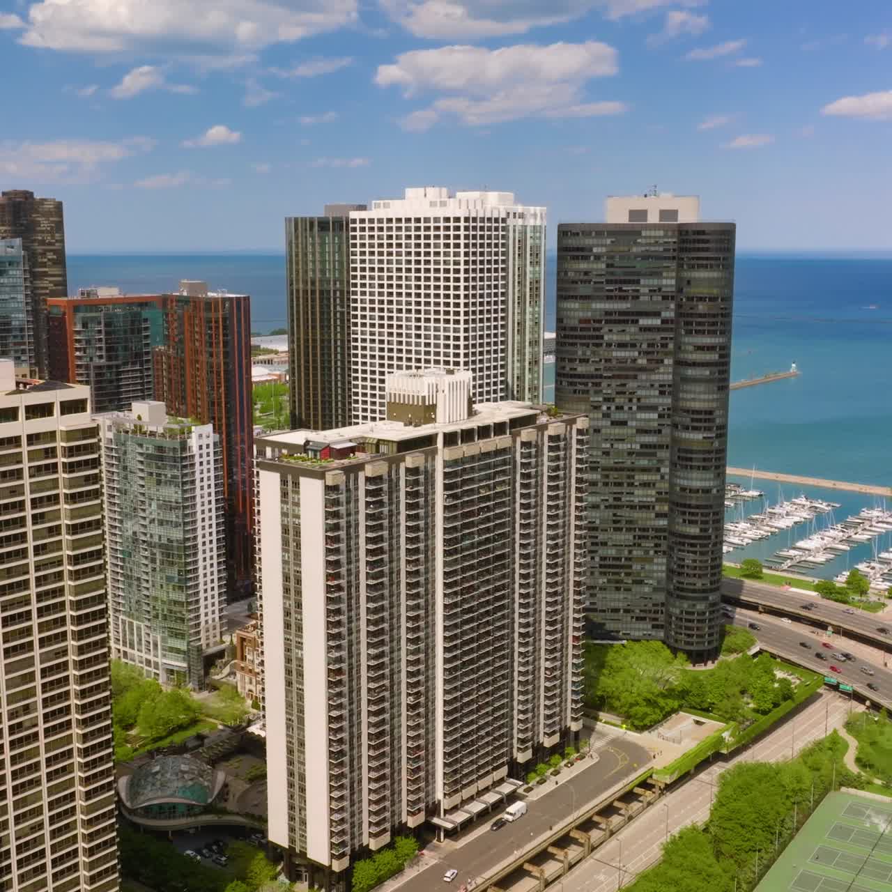 Huge high rise buildings and skyscrapers towering over busy traffic roads and yacht club. Eye-catching scenery of Chicago architecture at backdrop of blue horizon