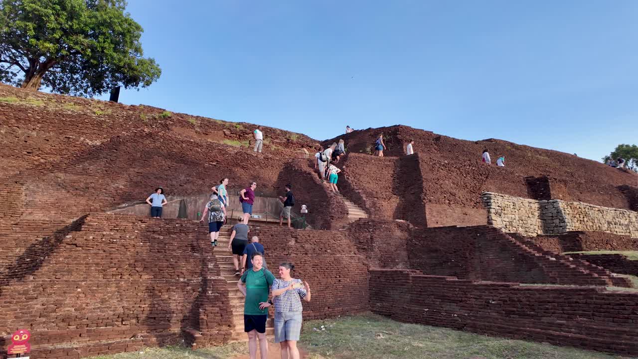 Tourists exploring and climbing the historic Sigiriya Lion Rock in Sri Lanka under a clear blue sky.