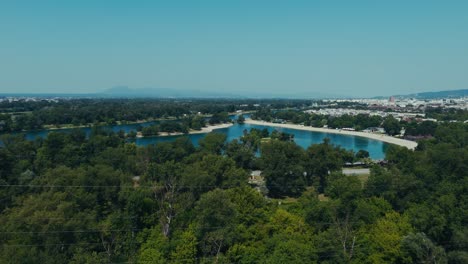 aerial - dense green forest in zagreb with view of lake jarun and urban skyline in summer