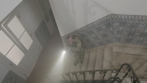 long shot of a focused soldier with scratches on face looking up and climbing stairs with flashlight