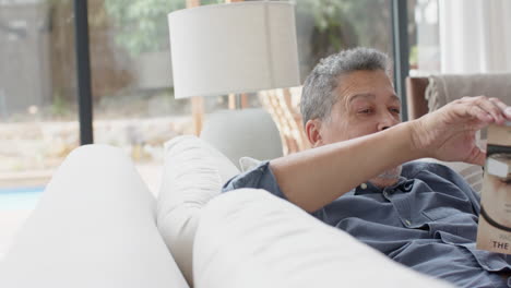 hombre de dos razas feliz relajándose en el sofá leyendo un libro en la sala de estar, espacio de copia, cámara lenta