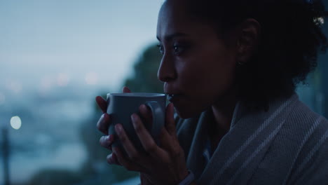 happy young woman looking out window drinking coffee enjoying cold early morning feeling cozy at home
