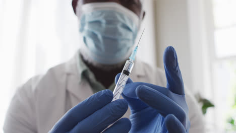 médico afroamericano masculino con máscara facial tocando burbujas de la jeringa