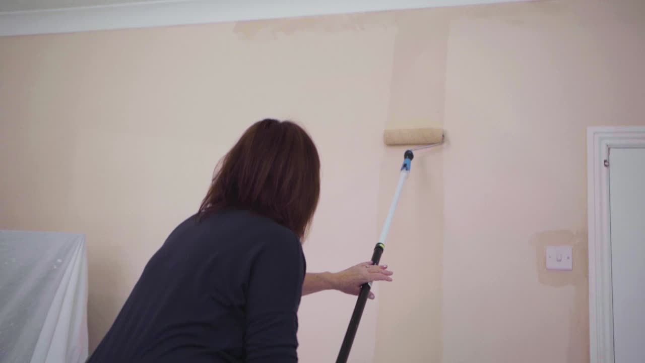 Woman painting a living room wall at home - using a paint roller (Medium shot) [Slow Motion]