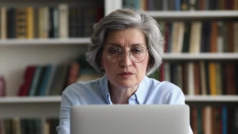 primer plano de una mujer mayor sonriente con gafas trabajando en una computadora portátil