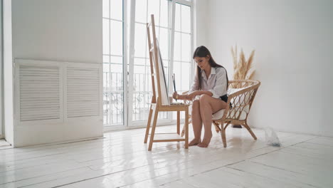 barefoot woman works with paints on wooden easel in studio