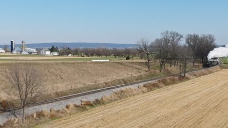 A-Drone-View-of-an-Antique-Steam-Passenger-Train,-Approaching,-Blowing-Smoke,-While-Traveling-Thru-Farmlands,-on-a-Sunny-Fall-Day