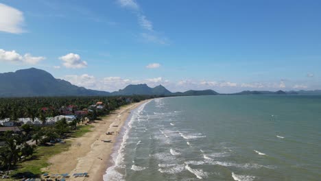 aerial steady footage of the beach and the landscape, waves rushing towards the shore, boats and some people, coconut trees
