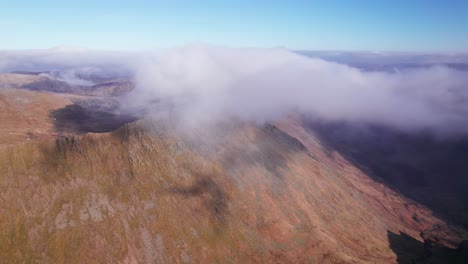 Disparo-De-Drone-Tirando-Hacia-Atrás-A-Través-De-Las-Nubes-Sobre-Una-Montaña,-Helvellyn,-Distrito-De-Los-Lagos,-Cumbria,-Reino-Unido