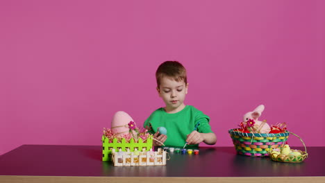 joyful small kid painting eggs for easter holiday festivity in studio