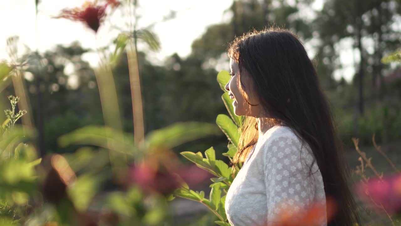 niña con gafas y vestido blanco girando y sonriendo muy feliz en un campo de flores de zinnia, durante la puesta de sol